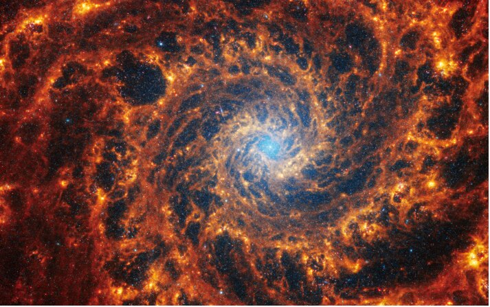 Spiral galaxy NGC 628 with light blue core and orange outer arms. 