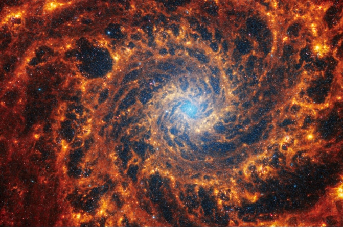 Spiral galaxy NGC 628 with light blue core and orange outer arms. 