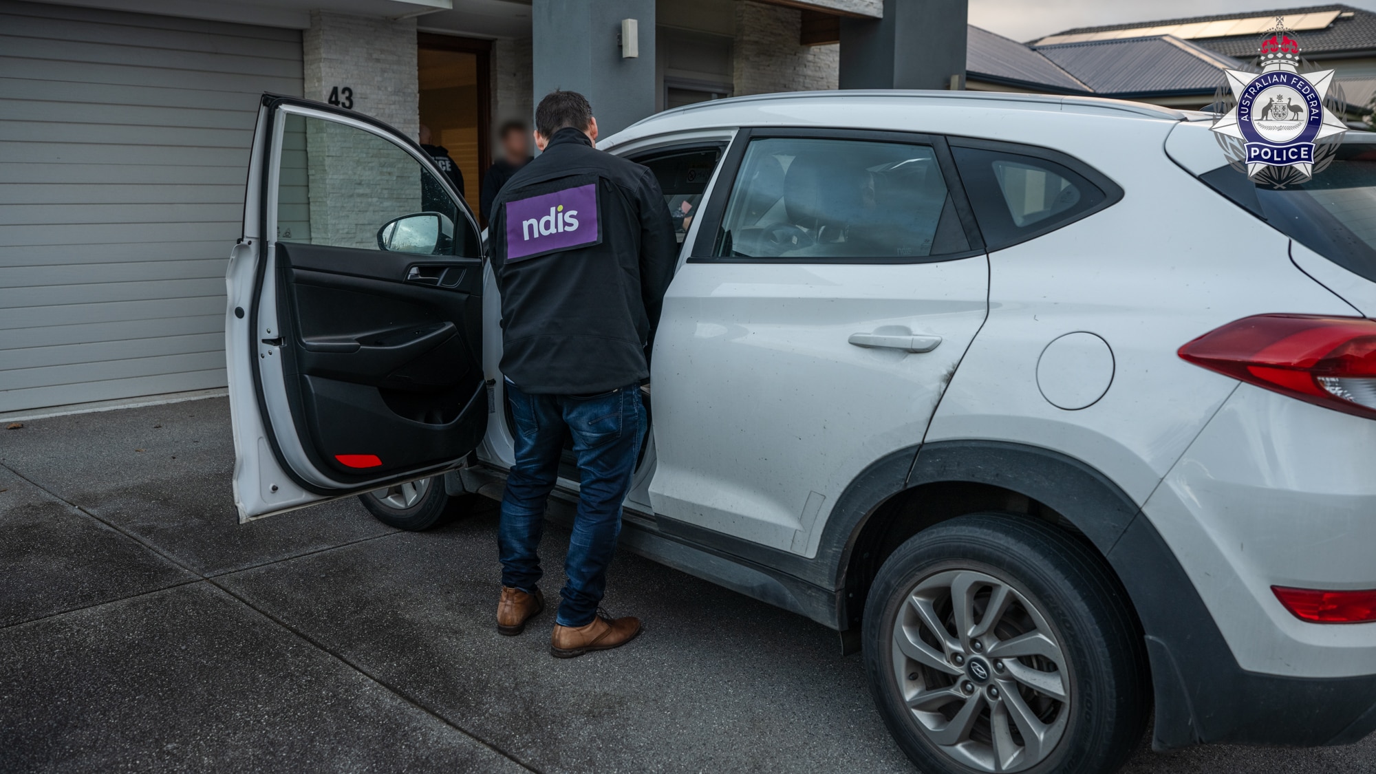 A person with NDIS on their back looks in a white small four-wheel drive