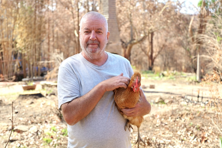 a man smiles at a camera holding a brown chicken.