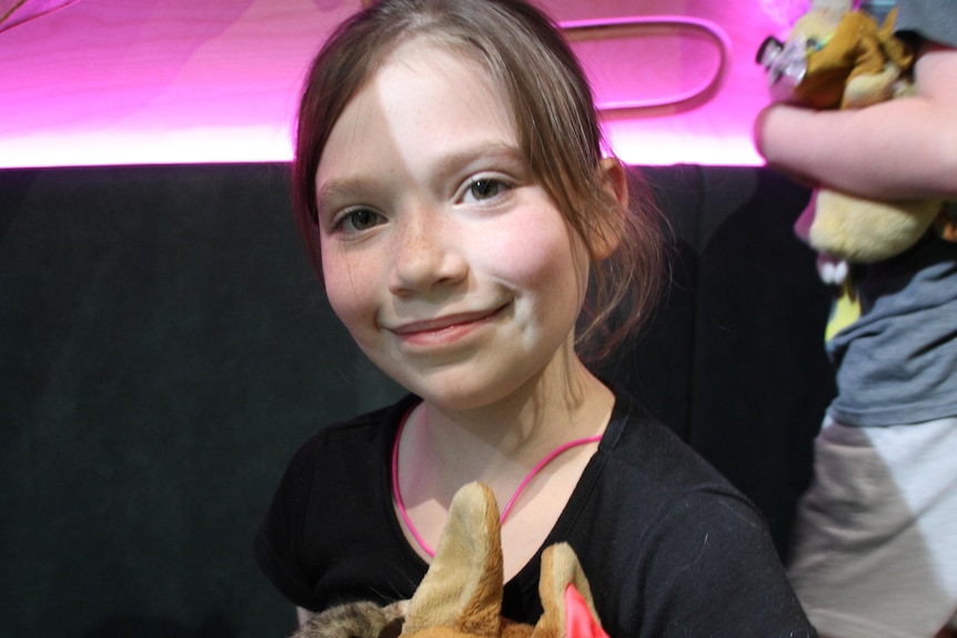 A little girl smiles holding some soft toys.