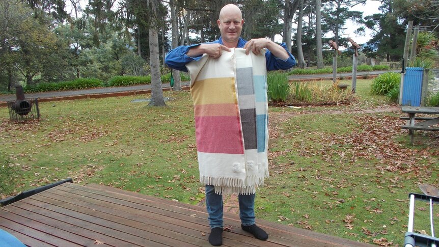 A man holding three woollen blankets at the front of his farm in the Coal River Valley