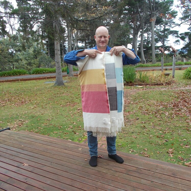 A man holding three woollen blankets at the front of his farm in the Coal River Valley