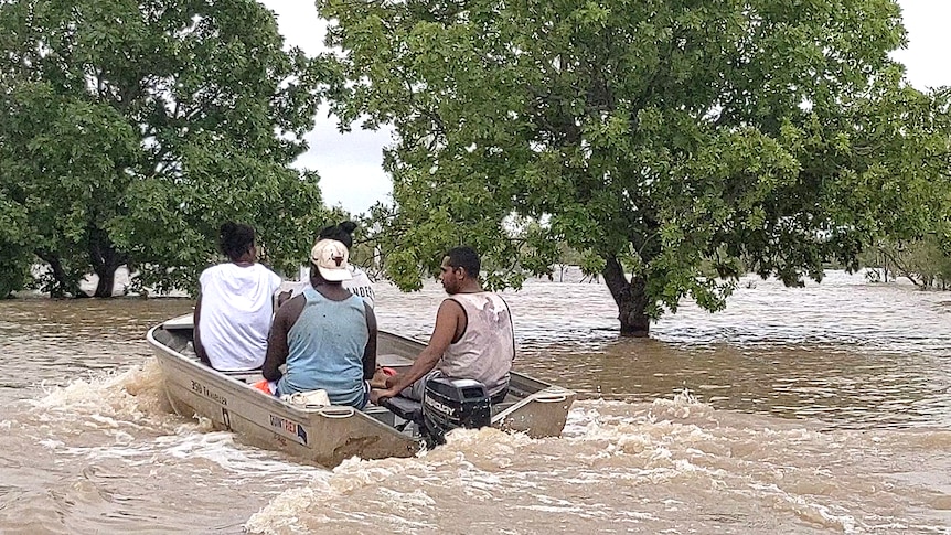 Four people in a small boat motoring through a badly flooded town.