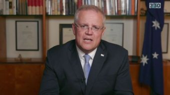 Scott Morrison speaks, looking at the camera, in his office, with an Australian flag in the background.