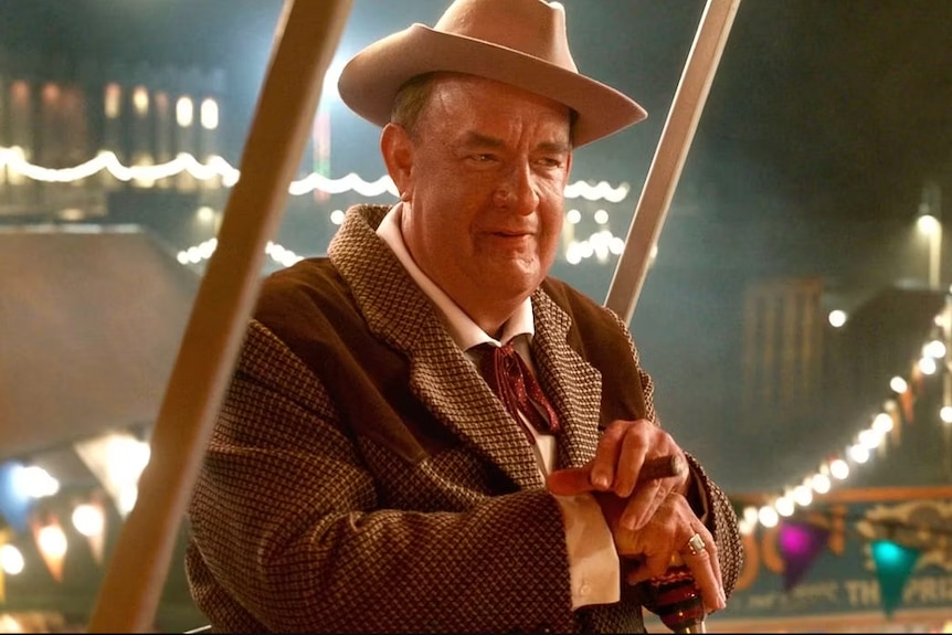 A puffed-up-looking, vaguely recognisable Tom Hanks smokes a cigar in an old suit while wearing a cowboy hat.