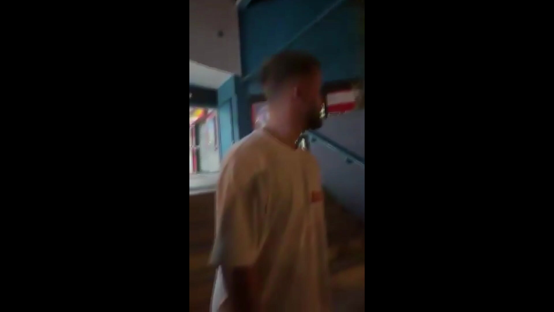 Screengrab of a man in a white t-shirt on the street at night.