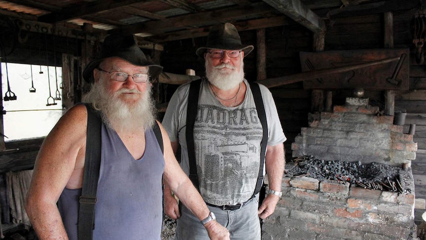Bill Kane and John Brown stand beside a home-made forge in a shed in Scottsdale in northern Tasmania.