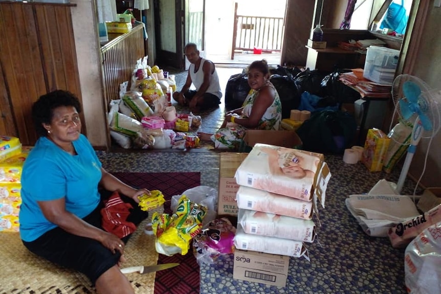 Two women and a man sit down on the floor surrounded by parcels.
