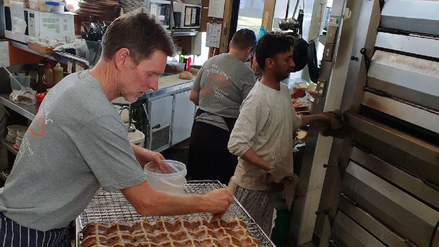 A male baker shapes dough into rectangle shapes on a bench inside a bakery.