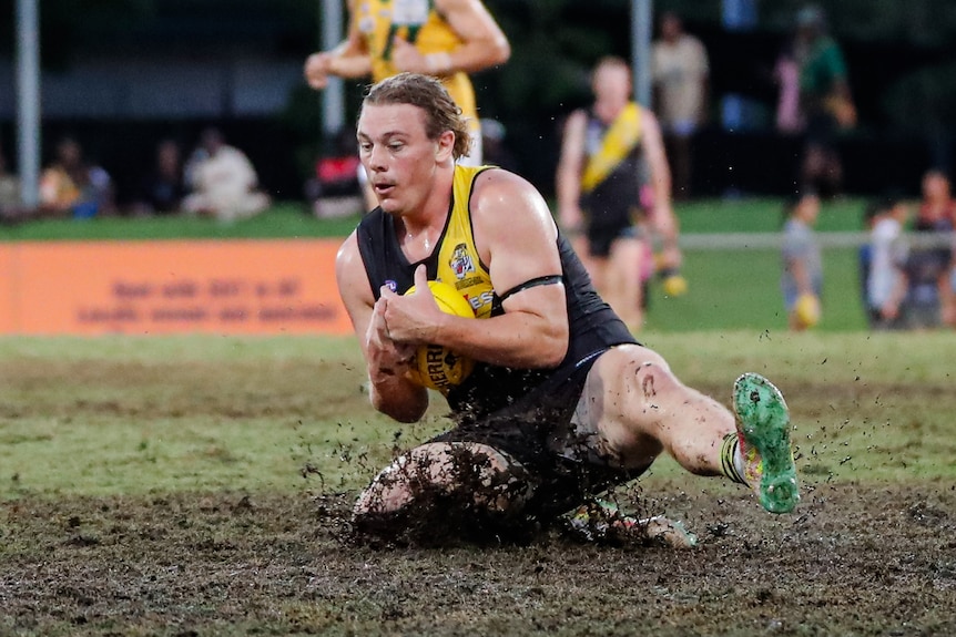 a man taking a mark in a football game, splashing in mud.