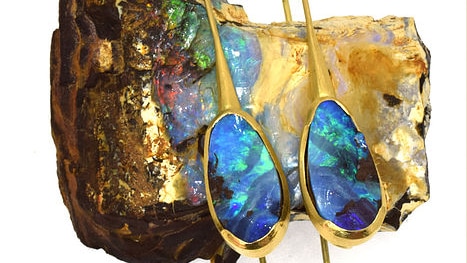Two opal earrings sitting on a raw opal