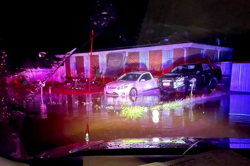 A photo at night captures two cars in a flooded driveway of a home.
