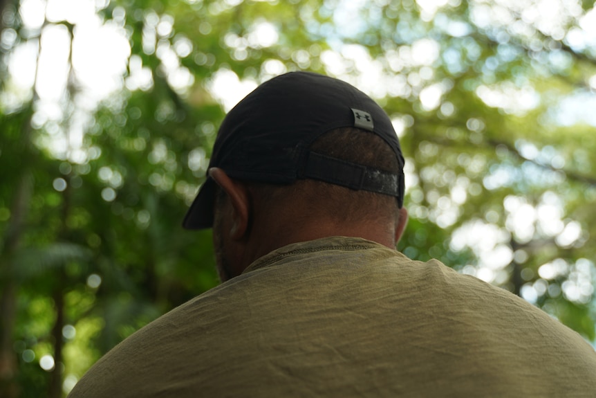 Man who has overcome heroin dependence, from behind wearing a cap and trees in front of him