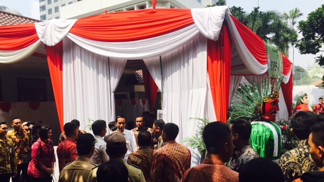 Indonesian President Joko Widodo stands in front of a voting booth covered in red and white cloth curtains.