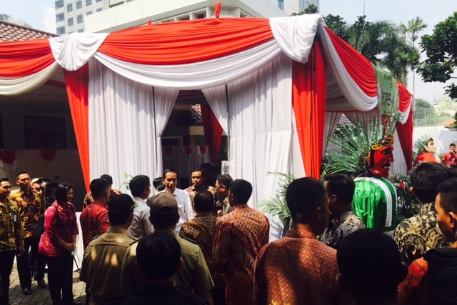 Indonesian President Joko Widodo stands in front of a voting booth covered in red and white cloth curtains.