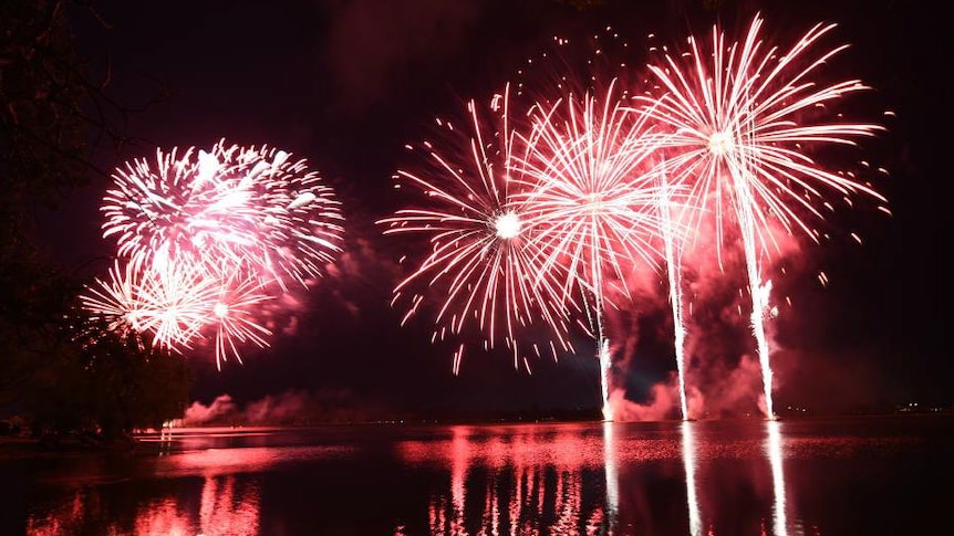 Red fireworks shooting up and exploding over a body of water at night