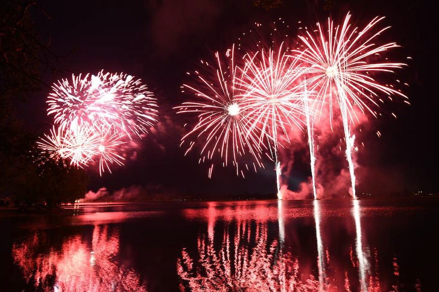 Red fireworks shooting up and exploding over a body of water at night