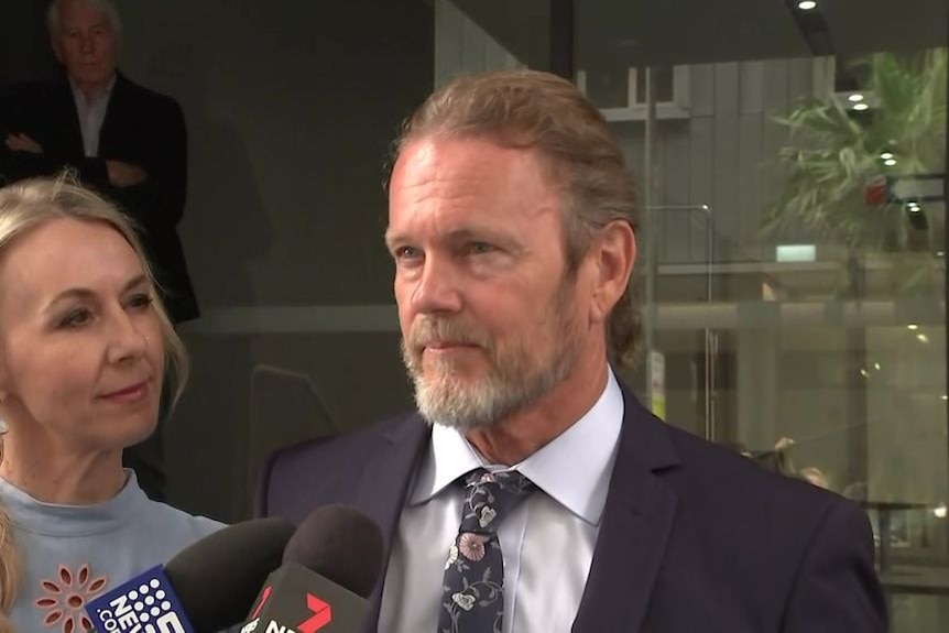 Craig McLachlan, flanked by his partner Vanessa Scammell, speaks to a group of journalists outside a Sydney building.