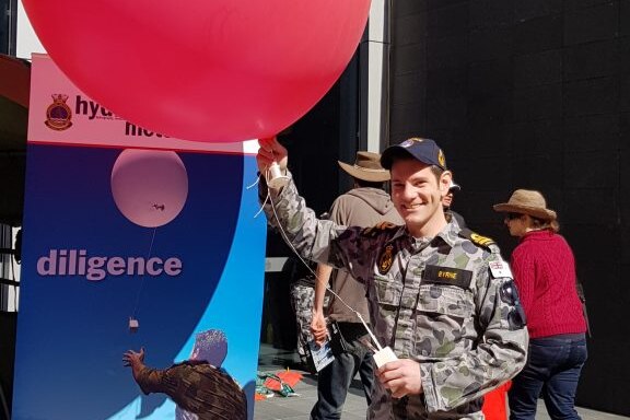 Man in uniform holding weather equipment and red balloon.