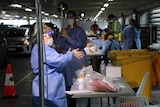 Healthcare workers in PPE stand around tables filled with testing materials