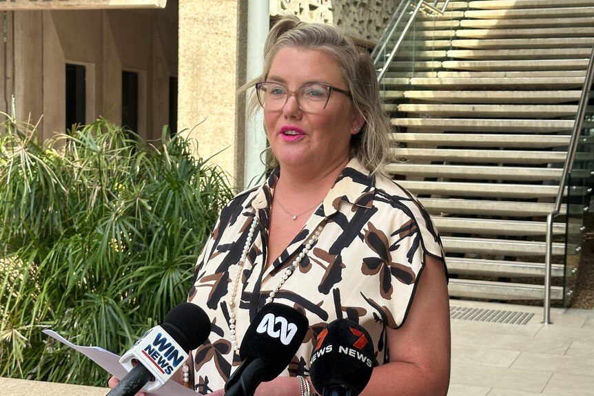 A blonde, bspectacled woman speaks to the media outside a court building.