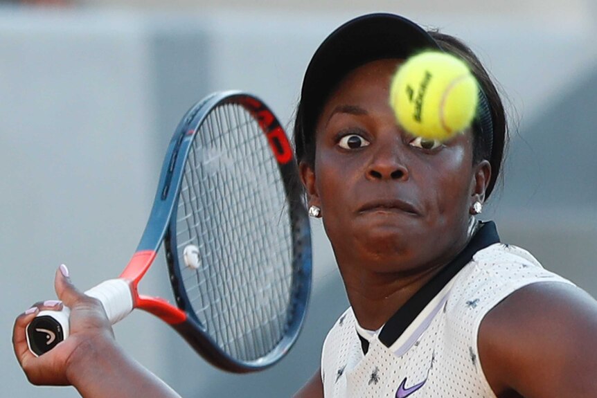 Sloan Stephens watches a tennis ball in front of her face with her racquet pulled back next to her head ready to hit the ball.