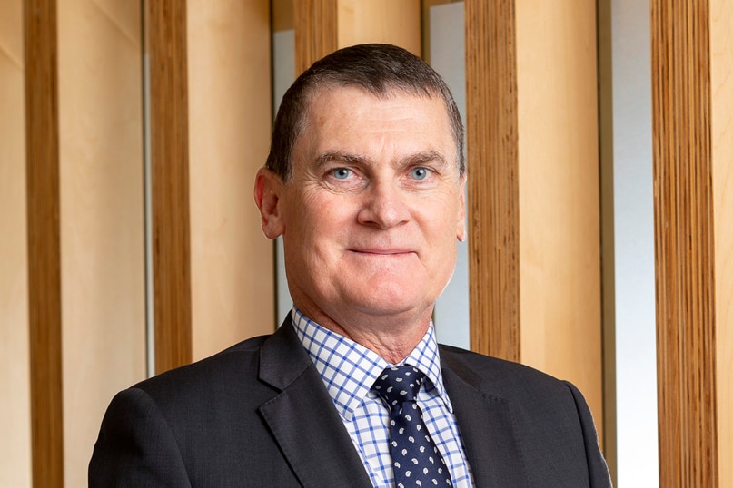 A man in a suit standing in front of a wood panel wall