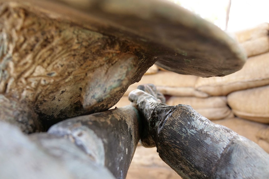 a statue of a man staring down the barrel of a rifle and aiming through a small opening in a sandbag barrier