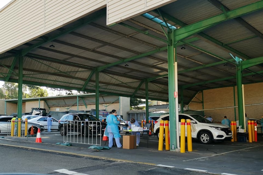 Cars line up at table where people in scrubs and masks stand with testing kits.