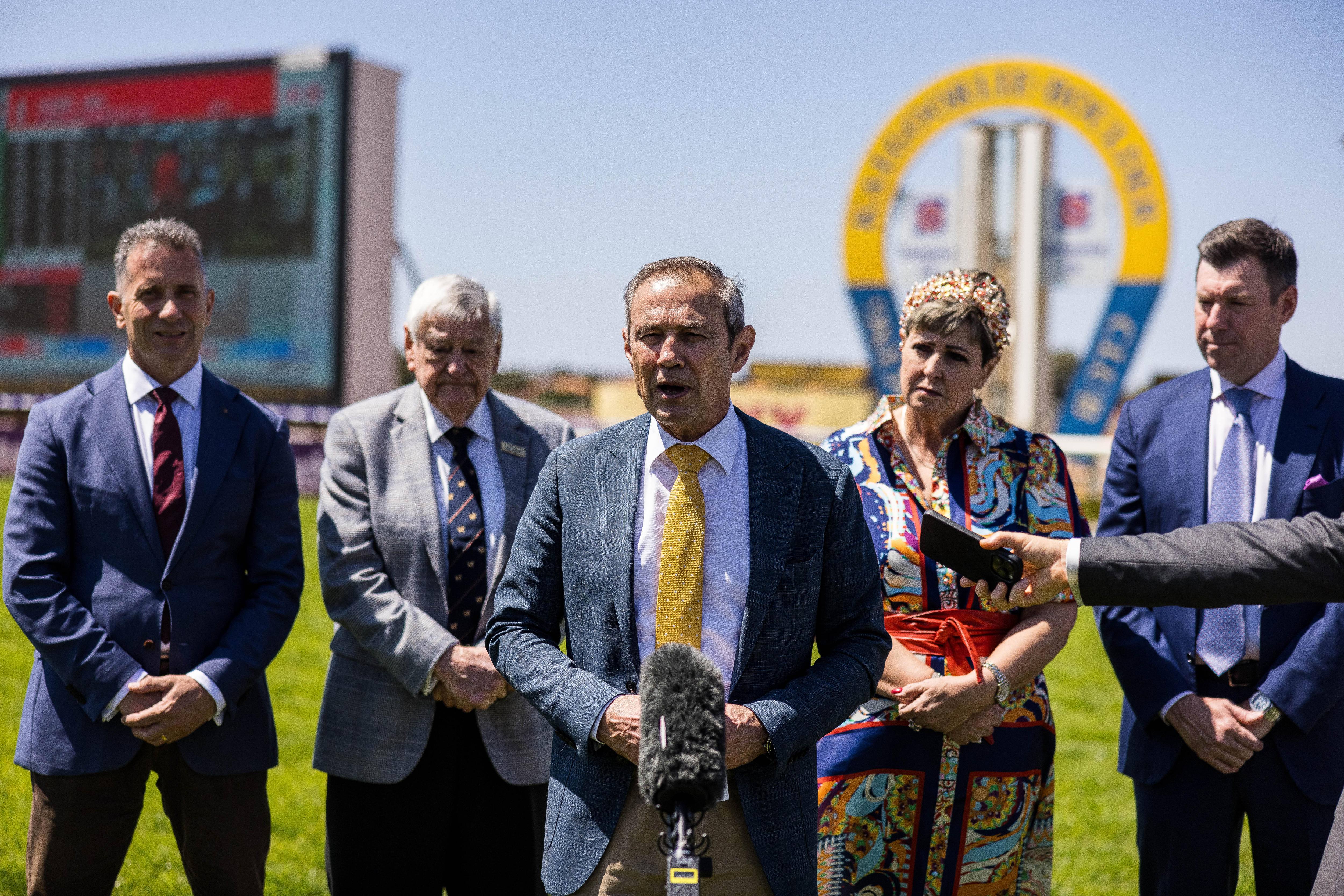 Un político de traje en una conferencia de prensa con cuatro personas detrás de él.  