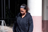 a woman in dark hoodie walks with her head down