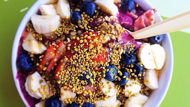 An acai bowl bowl held out by a hand, photographed from above.