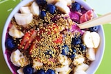An acai bowl bowl held out by a hand, photographed from above.