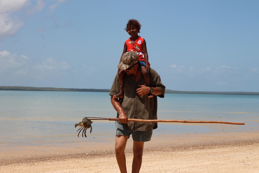 A man and his daughter walking on the beach.