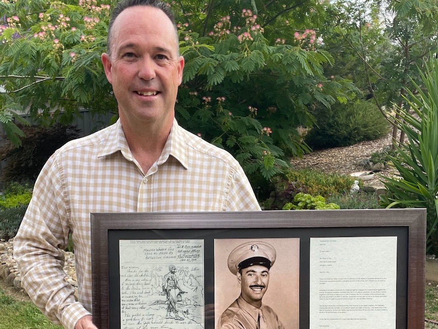 A man holds a three picture frame with two handwritten letters and a sepia image of a WWII US soldier.