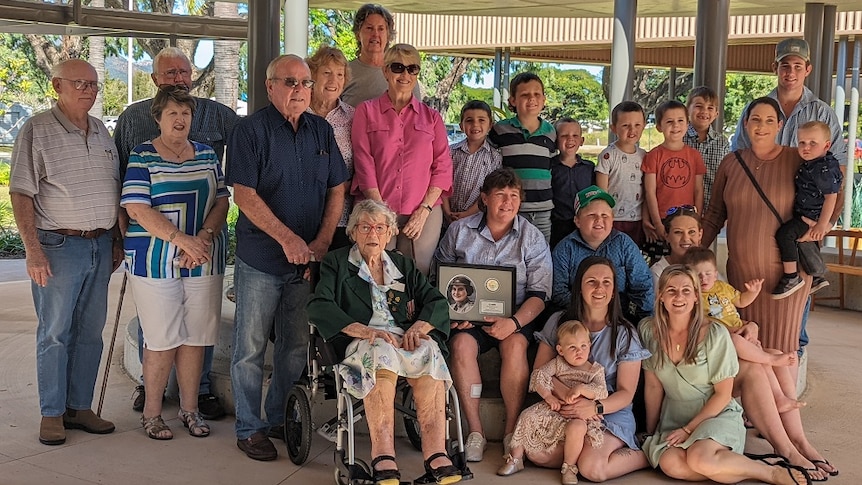 Lilian Somers sits in a wheel chair surrounded by her family with a plaque that has been dedicated to her