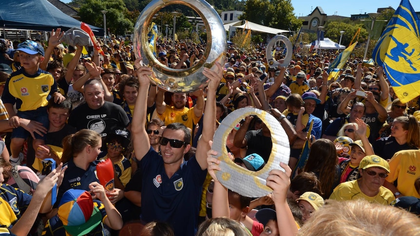 A man raises a circle-shaped trophy surrounded by hundreds of fans.