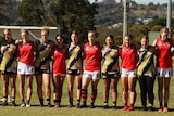 A line of girls with their arms around each other about to play a game of AFL. 