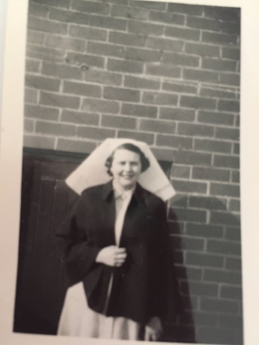 A black and white image of a woman wearing a white nurses bonnet and dark coat.