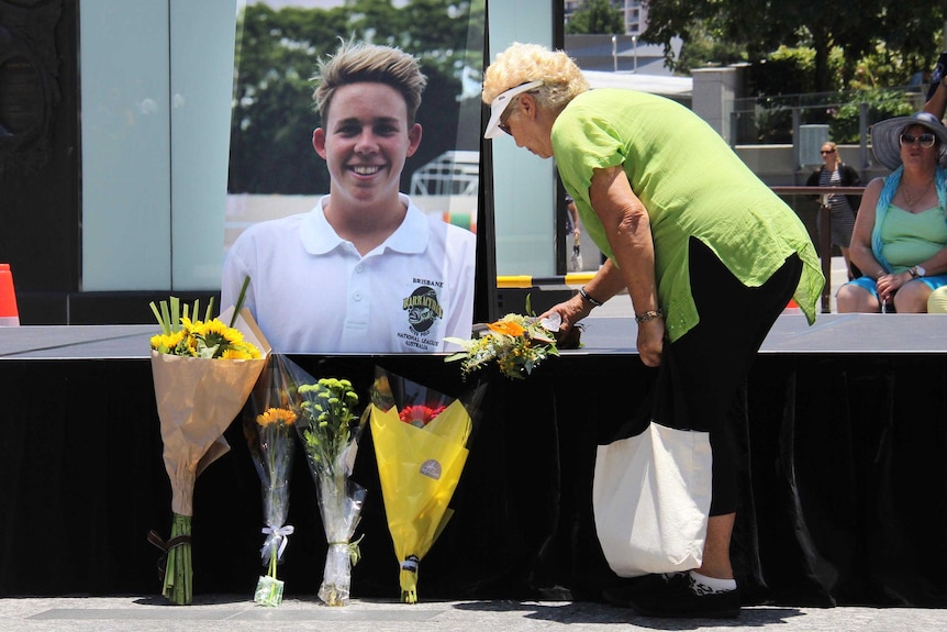 A woman lies flowers next to a photo of Cole Miller on the base of the podium at a memorial for coward punch victim.