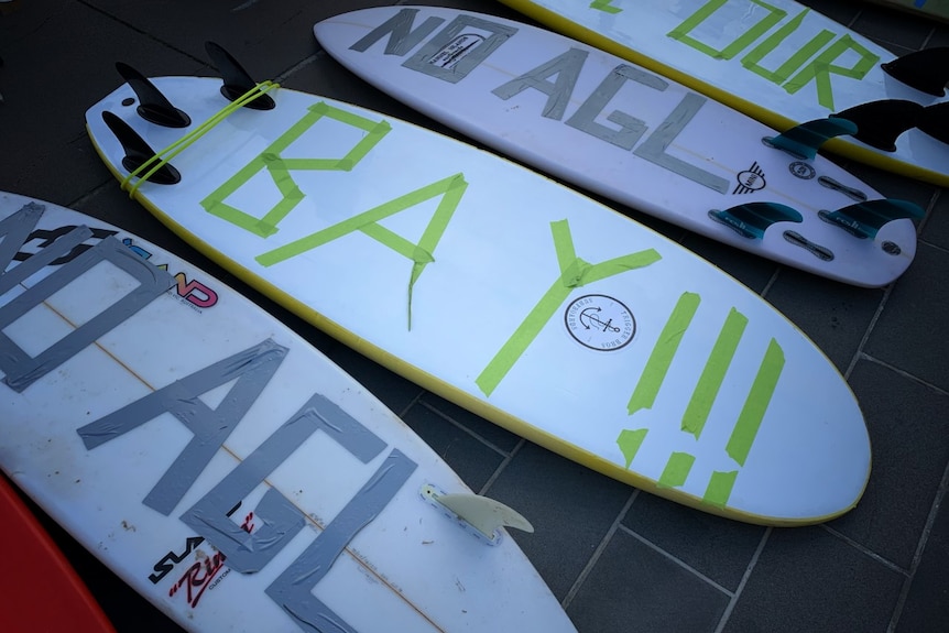 Surfboards bearing the words 'NO AGL' are laid down on the pavement outside Parliament House.