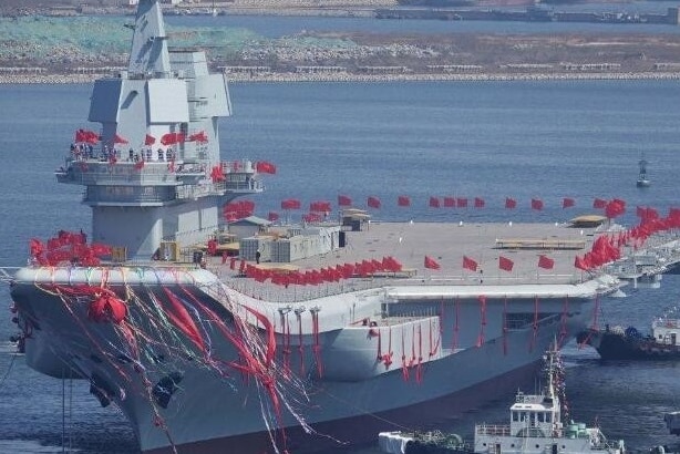 Chinese aircraft carrier Type 001A sailing, red flags flying on the carrier.