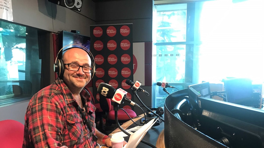 White man in a radio studio smiling at camera