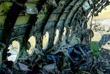 A burned out hull of a plane, with melted plastic clumped on the interior and mounds of debris on the ground.