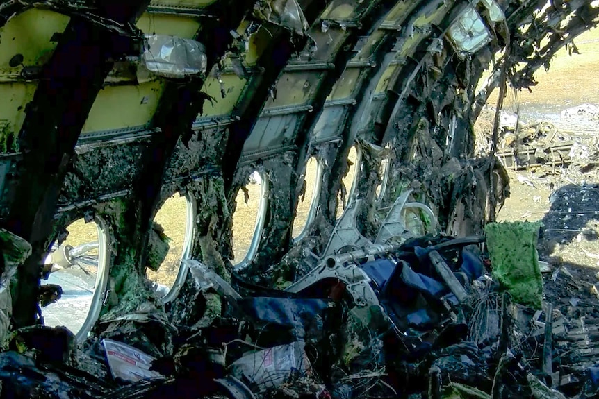 A burned out hull of a plane, with melted plastic clumped on the interior and mounds of debris on the ground.