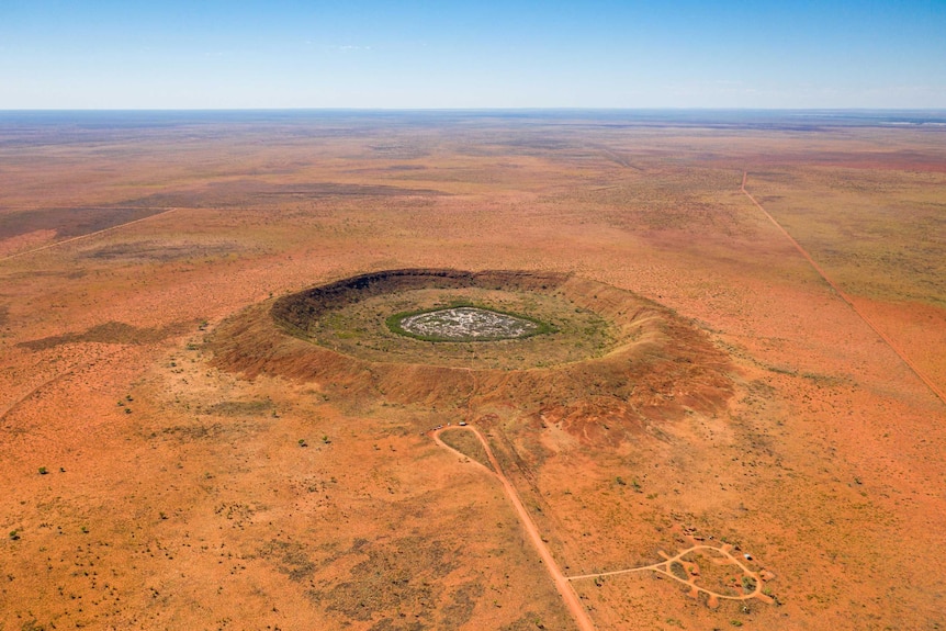 A large meteorite crater in the middle of an orange-coloured desert.