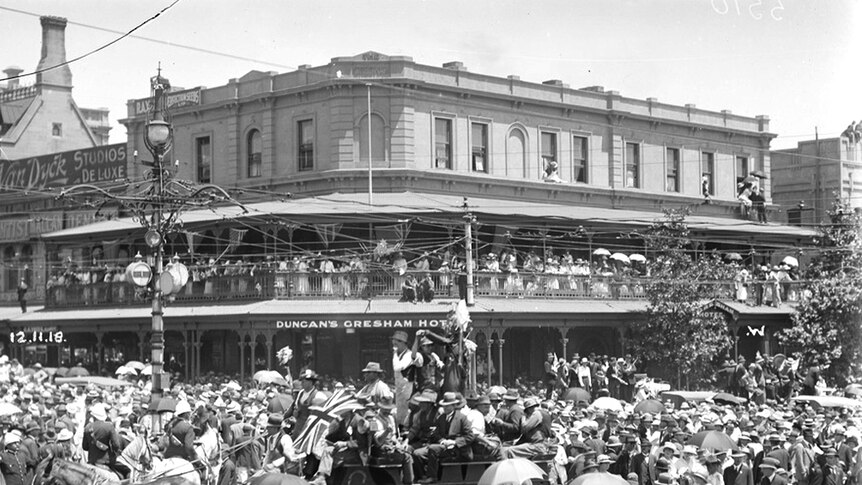 A large crowd of people gathered in Adelaide outside 'Duncan's Gresham Hotel'. A parade is going through the middle.