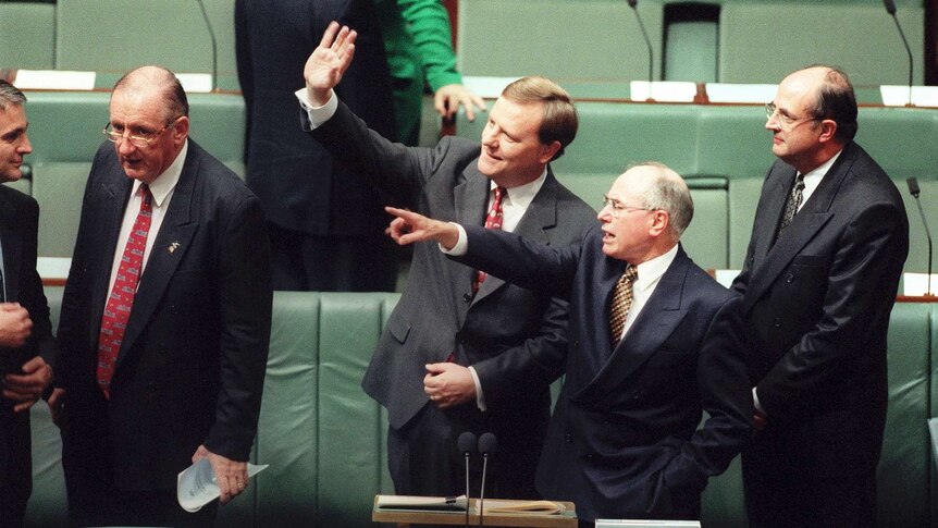 Five men in dark suits stand near the green front bench of the lower house