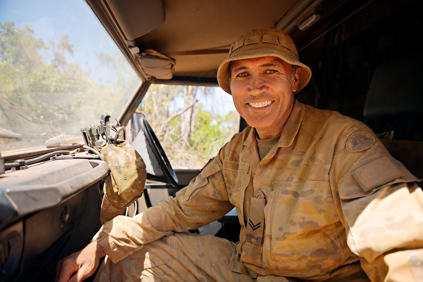 a man wearing army uniform smiling inside a military vehicle